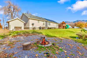 Rear view of house with an outdoor fire pit, a lawn, an outbuilding, stucco siding, and a mountain view