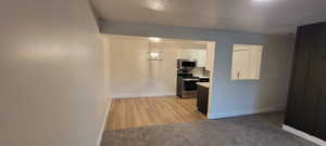 Kitchen featuring light countertops, appliances with stainless steel finishes, white cabinetry, light carpet, and decorative light fixtures