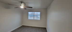 Empty room featuring dark colored carpet and a ceiling fan