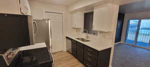 Kitchen featuring appliances with stainless steel finishes, white cabinetry, light countertops, light wood-type flooring, and dark cabinetry