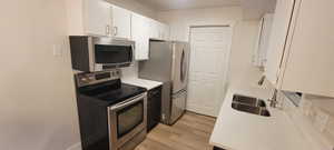 Kitchen with appliances with stainless steel finishes, decorative backsplash, white cabinetry, and light wood finished floors