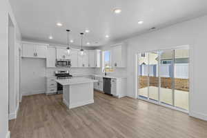 Kitchen featuring white cabinets, stainless steel appliances, decorative light fixtures, a center island, and light wood-style floors