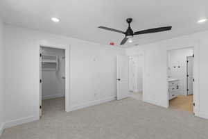 Unfurnished bedroom with light colored carpet, a spacious closet, recessed lighting, connected bathroom, and a ceiling fan