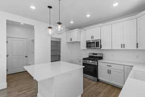 Kitchen with stainless steel appliances, a kitchen island, white cabinetry, decorative light fixtures, and tasteful backsplash