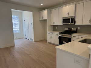 Kitchen with white cabinets, stainless steel appliances, light wood-type flooring, light stone countertops, and backsplash