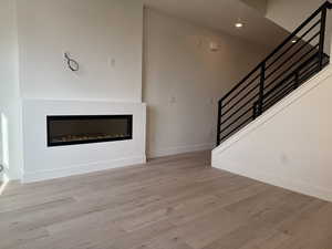 Unfurnished living room featuring stairs, light wood-style floors, a glass covered fireplace, and recessed lighting
