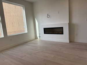 Unfurnished living room with a glass covered fireplace and light wood-style floors
