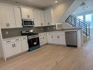 Kitchen featuring stainless steel appliances, white cabinets, light wood-style flooring, tasteful backsplash, and recessed lighting