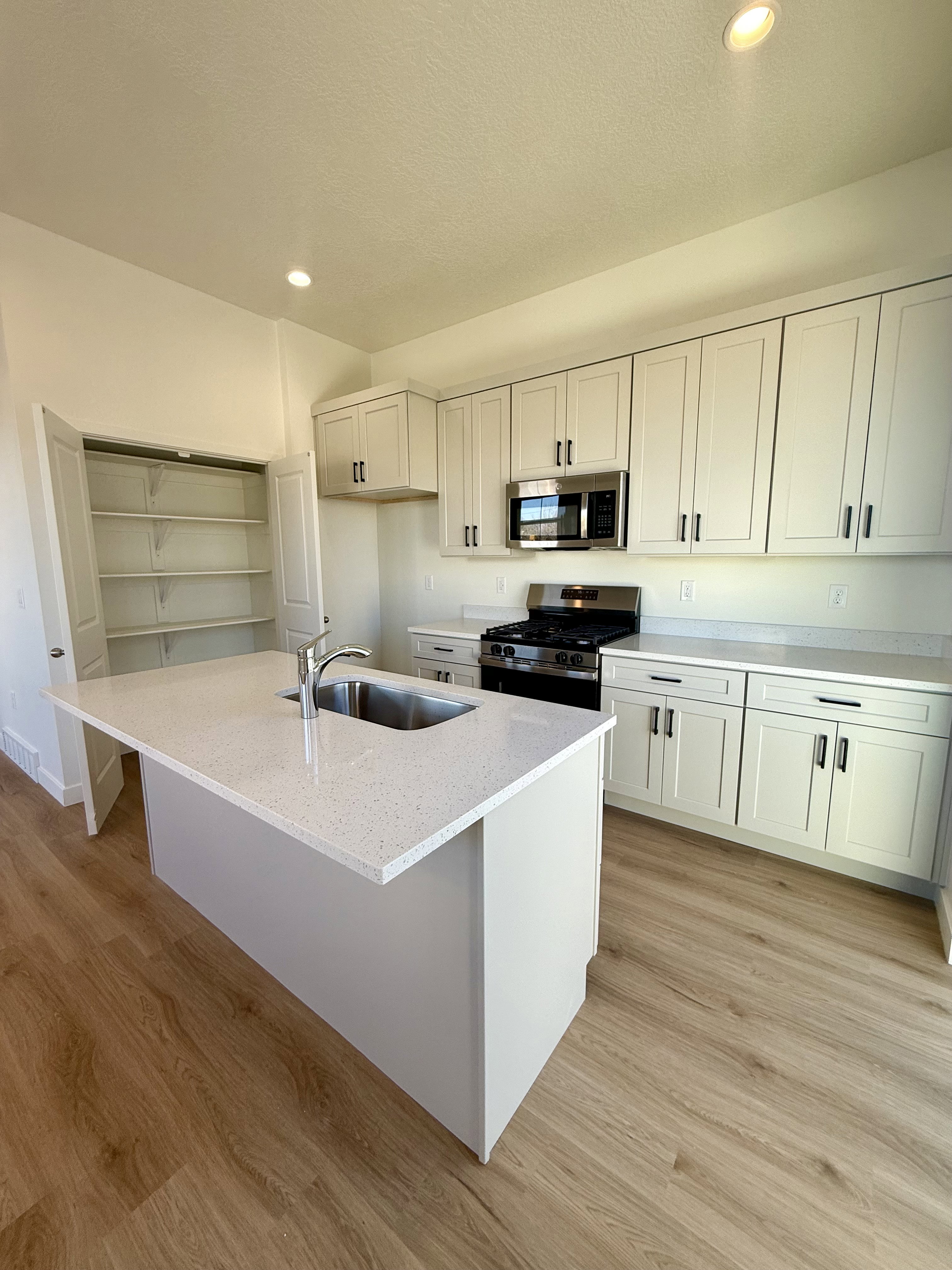 Kitchen with recessed lighting, stainless steel appliances, light stone countertops, a kitchen island with sink, and light wood-type flooring