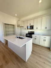 Kitchen with recessed lighting, stainless steel appliances, light stone countertops, a kitchen island with sink, and light wood-type flooring