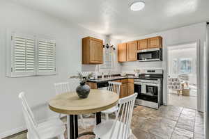 Kitchen with stainless steel appliances, dark countertops, brown cabinets, and light stone finish flooring