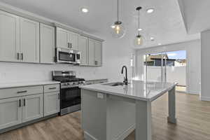 Kitchen featuring appliances with stainless steel finishes, pendant lighting, a kitchen island with sink, light wood-style flooring, and decorative backsplash