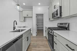 Kitchen featuring stainless steel appliances, pendant lighting, light wood-type flooring, backsplash, and light stone counters
