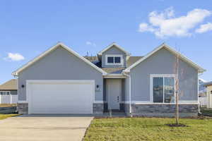 View of front of home featuring stone siding, stucco siding, driveway, a front yard, and a garage