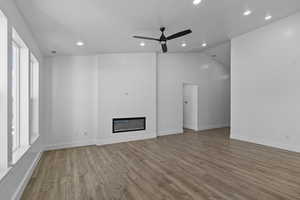 Unfurnished living room with a glass covered fireplace, wood finished floors, recessed lighting, a ceiling fan, and vaulted ceiling