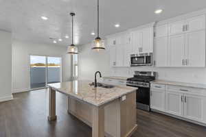 Kitchen featuring stainless steel appliances, a center island with sink, decorative backsplash, light stone countertops, and white cabinets