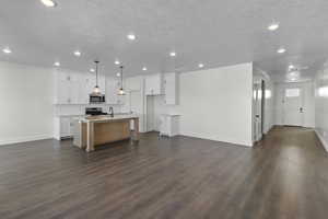 Kitchen featuring open floor plan, white cabinets, a center island with sink, range, and stainless steel microwave