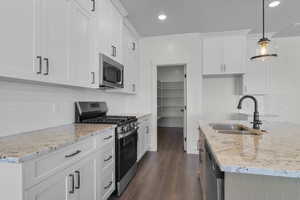 Kitchen featuring stainless steel appliances, white cabinetry, light stone counters, dark wood-style floors, and recessed lighting