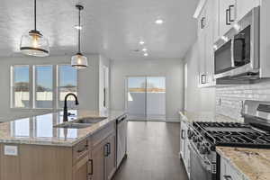 Kitchen with appliances with stainless steel finishes, light stone countertops, decorative light fixtures, white cabinets, and recessed lighting