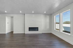 Unfurnished living room with a large fireplace, dark wood-style flooring, recessed lighting, and a textured ceiling