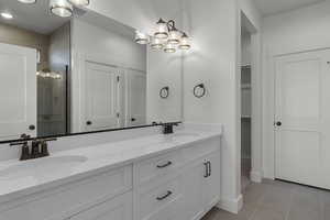Full bathroom featuring double vanity, a stall shower, light tile patterned flooring, a walk in closet, and a chandelier