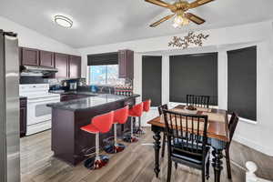 Kitchen featuring electric stove, stainless steel fridge, lofted ceiling, a kitchen bar, and a peninsula
