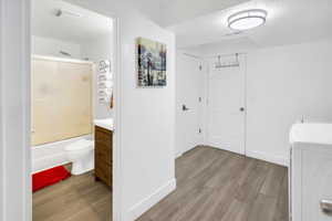 Full bathroom featuring vanity, light wood finished floors, shower / bath combination with glass door, a textured ceiling, and washer / dryer