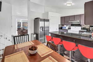 Kitchen with white appliances, vaulted ceiling, a kitchen bar, tasteful backsplash, and dark brown cabinets