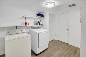 Laundry room with independent washer and dryer, a textured ceiling, and light wood-style flooring