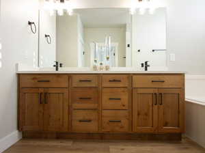 Master bathroom featuring a chandelier, double vanity, a tub, and light wood finished floors