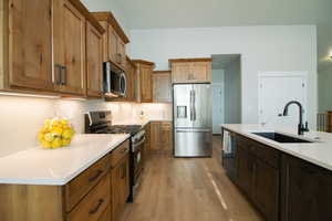 Kitchen featuring appliances with stainless steel finishes, light wood-style floors, light stone counters, and brown cabinets