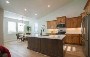 Kitchen with stainless steel appliances, recessed lighting, an island with sink, light wood-style flooring, and brown cabinets