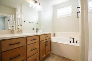 Master bathroom featuring vanity, a bath, and light wood-style flooring