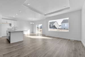 Kitchen featuring white cabinets, a chandelier, a kitchen island with sink, open floor plan, and hanging light fixtures