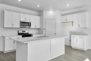 Kitchen with stainless steel appliances, white cabinetry, light wood-style floors, a kitchen island with sink, and recessed lighting