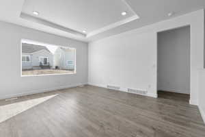 Empty room with light wood-style floors, recessed lighting, and a tray ceiling