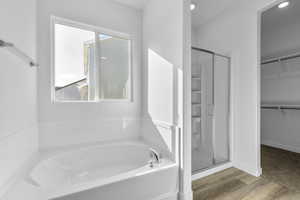 Full bath featuring a bath, a walk in closet, a shower stall, and wood finished floors