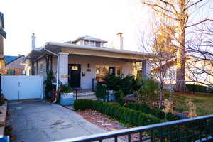View of front of property featuring a porch, a chimney, brick siding, and a gate