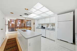Kitchen featuring white appliances, white cabinetry, light floors, light countertops, and a center island