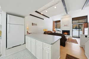 Kitchen with freestanding refrigerator, white cabinetry, a peninsula, light countertops, and a warm lit fireplace