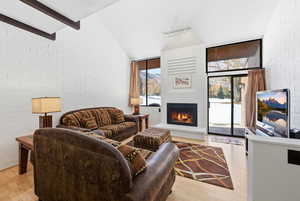 Living room featuring brick wall, a fireplace, light wood-style floors, and high vaulted ceiling