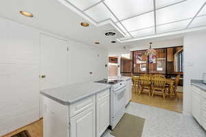 Kitchen featuring white cabinetry, white range with electric cooktop, pendant lighting, a kitchen island, and light countertops