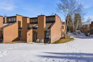 Snow covered property featuring a patio, brick siding, and a chimney