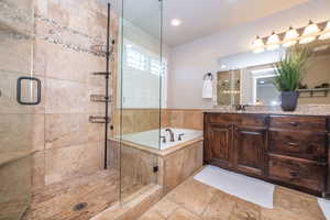 Full bath featuring vanity, a garden tub, a stall shower, stone tile floors, and recessed lighting