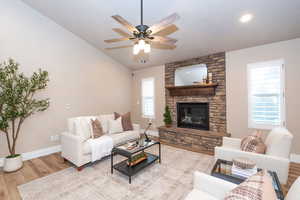 Living room with wood finished floors, a fireplace, vaulted ceiling, and a ceiling fan