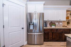 Kitchen with stainless steel appliances, dark brown cabinetry, white cabinets, and tasteful backsplash
