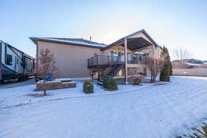 Snow covered back of property with a patio area, stairway, stucco siding, and a deck