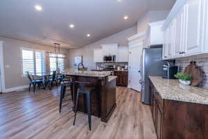 Kitchen with an island with sink, white cabinets, a breakfast bar, lofted ceiling, and tasteful backsplash