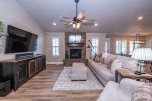 Living area featuring light wood-style floors, recessed lighting, ceiling fan, vaulted ceiling, and a stone fireplace