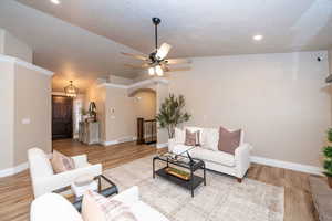 Living room featuring a ceiling fan, light wood-style floors, arched walkways, a textured ceiling, and recessed lighting